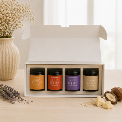 Set of four body butter jars in a box with decorative elements on a light surface.